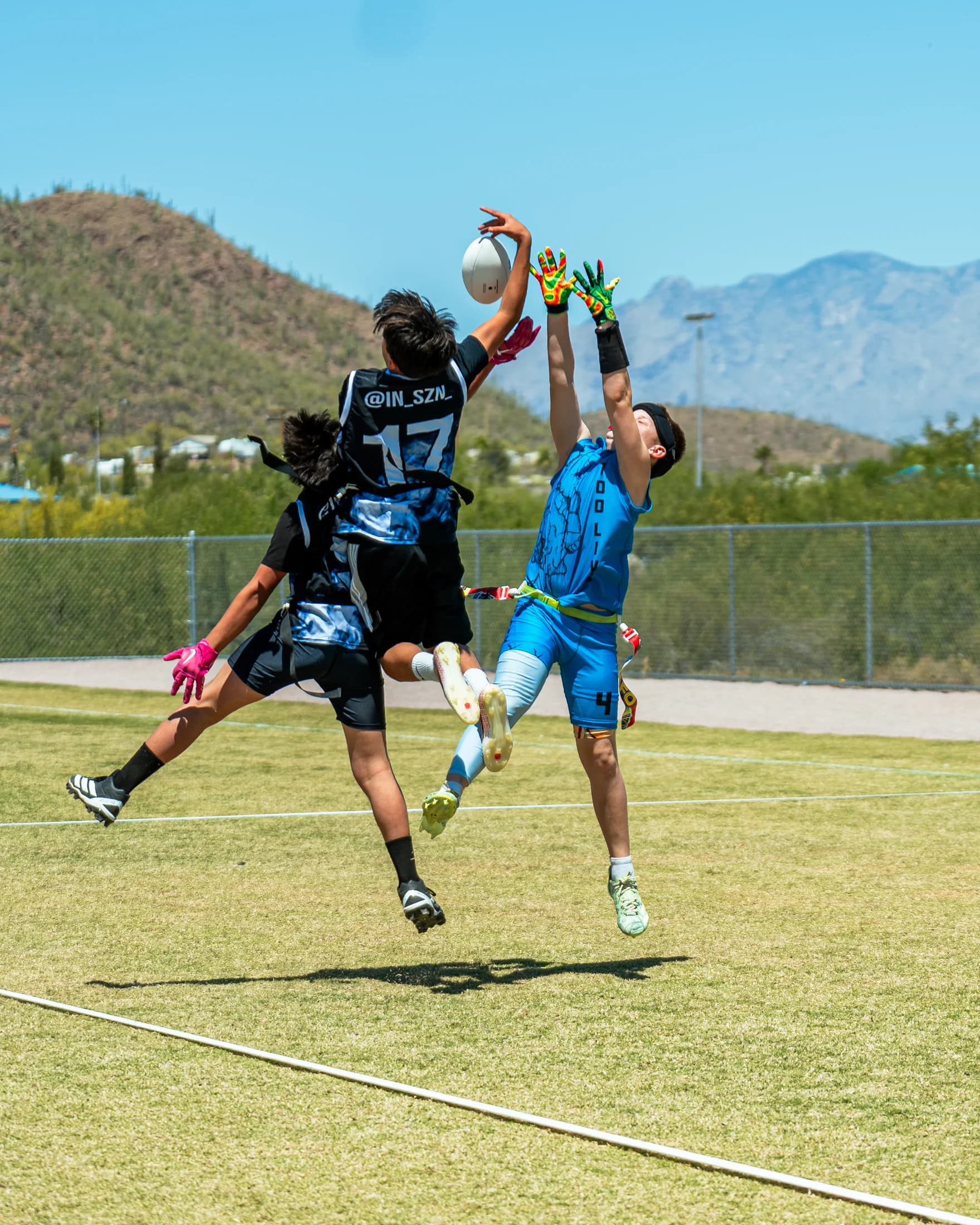 Three youth flag football players reaching for a pass with Tucson mountains behind them